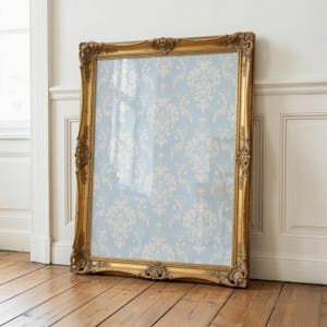 May include: A large rectangular mirror featuring an ornate, gilded gold frame with intricate carved detailing. The glass surface reflects a light blue background adorned with a repeating white damask pattern, creating a decorative visual effect.
