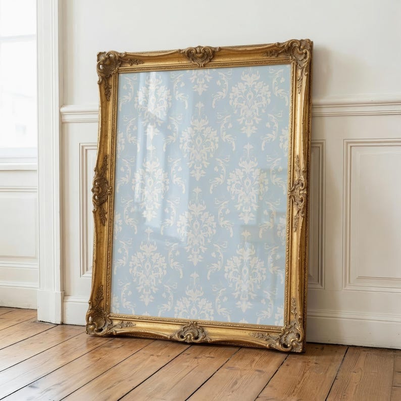 May include: A large rectangular mirror featuring an ornate, gilded gold frame with intricate carved detailing. The glass surface reflects a light blue background adorned with a repeating white damask pattern, creating a decorative visual effect.