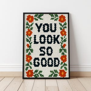May include: Framed art print with the words "YOU LOOK SO GOOD" in black, surrounded by a floral border of orange flowers and green leaves. The background is a mosaic pattern. The frame is black.