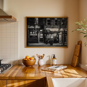 May include: A framed black and white photograph of a building with the neon sign "Cadillac Lounge" hanging above the entrance. The photograph is displayed in a kitchen setting with a wooden countertop and a gas stove.