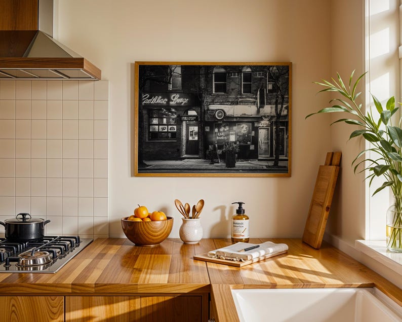 May include: A framed black and white photograph of a building with the neon sign "Cadillac Lounge" hanging above the entrance. The photograph is displayed in a kitchen setting with a wooden countertop and a gas stove.