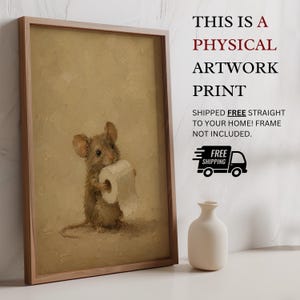 May include: A framed artwork print featuring a brown mouse holding a roll of white toilet paper against a textured beige background. The print is displayed next to a small white vase. The text reads: THIS IS A PHYSICAL ARTWORK PRINT.