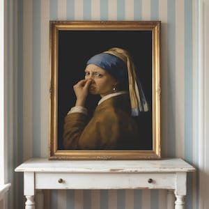 May include: A framed oil painting depicting a person wearing a blue headscarf and a brown jacket, holding their nose with one hand. The figure is set against a dark background and is encased in an ornate gold frame with intricate detailing.