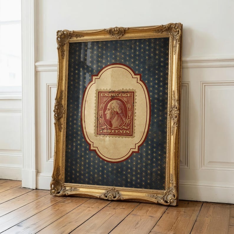Op de afbeelding: Een ingelijste vintage Amerikaanse postzegel met George Washington, tegen een marineblauwe achtergrond met gouden sterpatronen. De postzegel zit in een decoratieve, sierlijke gouden lijst, leunend tegen een witte muur en een houten vloer.