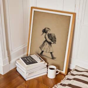 May include: A framed sepia-toned print featuring a sketch of a person walking while carrying a stack of books. The artwork is displayed in a light wood frame, positioned next to a stack of four books and a white ceramic mug filled with dark liquid.