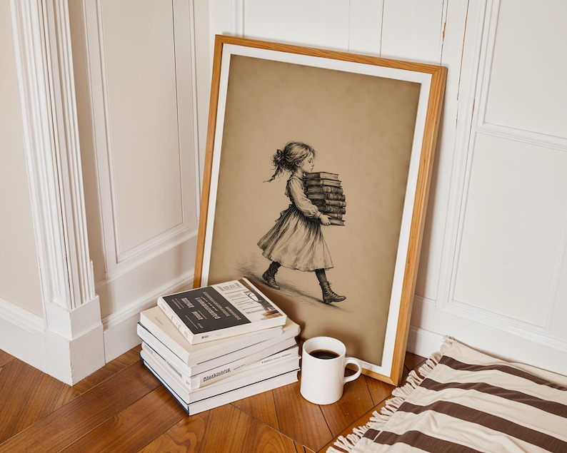 May include: A framed sepia-toned print featuring a sketch of a person walking while carrying a stack of books. The artwork is displayed in a light wood frame, positioned next to a stack of four books and a white ceramic mug filled with dark liquid.