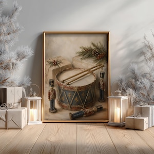 Puede incluir: Un cuadro enmarcado que representa un tambor antiguo con dos baquetas de madera encima, flanqueado por dos figuras de cascanueces de pie y una tumbada. La escena incluye cajas de regalo envueltas y ramas de pino en tonos neutros.