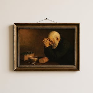 May include: A framed oil painting depicting an elderly person with a white beard and dark clothing sitting at a table with hands clasped in prayer. On the table sits a thick book, a small bowl, a knife, and a loaf of bread in dim lighting.