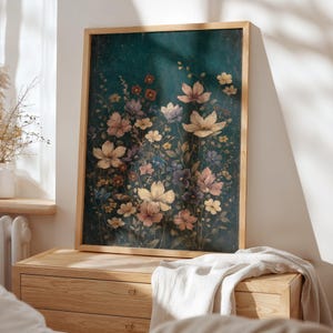 May include: A framed floral print featuring a variety of flowers in shades of cream, pink, purple, and yellow against a dark teal background. The artwork is displayed on a wooden dresser, with a white blanket draped over it.