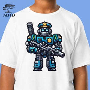 May include: White t-shirt with a cartoon robot police officer in blue and black, holding a gun. The robot wears a police hat and badge. The shirt also has the text "ABTD" in the upper left corner.