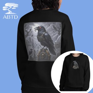 May include: Black sweatshirt featuring a detailed graphic of a raven with red eyes, perched on a tombstone in a gothic graveyard scene. The raven wears a spiked collar. The sweatshirt has the logo "ABTD" on the upper left.