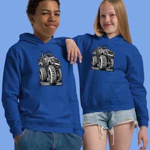 Op de afbeelding: Twee mensen dragen koningsblauwe hoodies. Elke hoodie heeft een zwart-witte afbeelding van een monstertruck met grote banden. De hoodies hebben een voorzak en een capuchon. De achtergrond is effen lichtblauw.