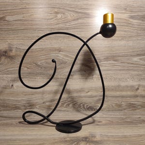 May include: Black metal candle holder shaped like the letter D with a gold candle on top.