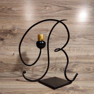 May include: Black metal candle holder shaped like the letter R. The holder has a single candle holder and a square base.