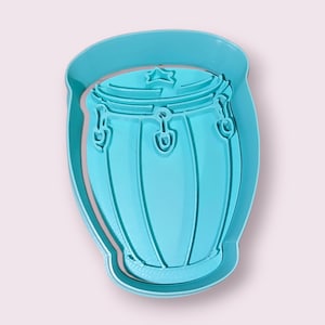 May include: A turquoise plastic cookie cutter in the shape of a conga drum. The cutter has a star detail on the top and is surrounded by a rounded border. The design is a musical instrument.
