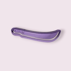 Puede incluir: Un cortador de galletas morado y curvado con forma de machete. El cortador tiene un mango con tres pequeños agujeros y una cuchilla con un borde decorativo. El diseño está hecho de un material sólido y liso.