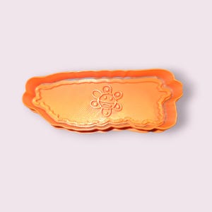 Puede incluir: Cortador de galletas naranja con la forma de Puerto Rico, con un diseño de sol sonriente en el centro. El cortador de plástico tiene un borde festoneado. Ideal para hacer galletas u otras golosinas.