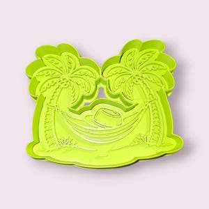 以下が含まれることがあります： ヤシの木が2本、その間にハンモックが張られた形のライムグリーンのクッキーカッター。ハンモックには帽子が置かれています。トロピカルまたは休暇をテーマにしたクッキー作りに適したデザインです。