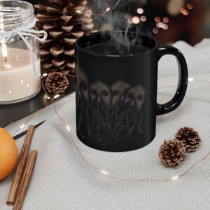 May include: Black ceramic coffee mug with a graphic of multiple tentacled creatures with eyes. The mug is filled with coffee and steam is rising from the mug.