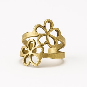 Könnte beinhalten: Ein goldfarbener Ring mit zwei durchbrochenen Blumenmustern. Der Ring hat einen Wickelstil, wobei sich die floralen Elemente oben und an der Seite befinden. Der Ring besteht aus glänzendem Metall.