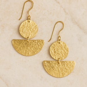 Könnte beinhalten: Ein Paar goldfarbene Ohrringe. Jeder Ohrring hat ein strukturiertes, kreisförmiges Oberteil und ein strukturiertes, halbkreisförmiges Unterteil. Die Ohrringe haben einen Hakenverschluss. Der Hintergrund ist hell und neutral.