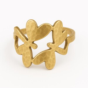 Könnte beinhalten: Ein goldfarbener Ring mit einem Schmetterlingsdesign. Der Ring hat eine strukturierte Oberfläche und ein Band. Das Schmetterlingsdesign besteht aus vier verbundenen Schmetterlingsformen.