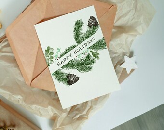May include: A white card with a green pine branch design and the text "Happy Holidays" in black lettering.