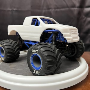 Op de afbeelding: Wit monstertruck-model met zwarte banden en blauwe velgen. De banden hebben het woord "BKT" erop gedrukt.