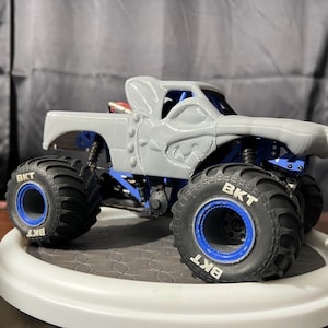 Op de afbeelding: Een grijze monstertruck met een aangepaste carrosserie en blauwe wielen. De wielen hebben de tekst "BKT" erop.