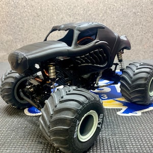 May include: Black monster truck with large tires and a detailed body. The truck has a black and white tire with the text "BKT" on the side.