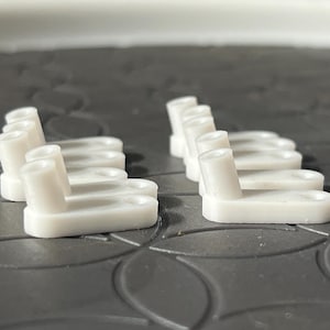 May include: A set of ten white plastic model parts, each with a small raised rectangular base and a vertical post. The parts are arranged in two rows of five, with the posts facing the same direction.