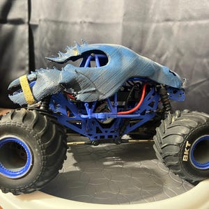 Op de afbeelding: Een blauwe en zwarte monstertruck met grote banden. De banden hebben het woord "BKT" erop gedrukt. De truck heeft een gedetailleerd carrosserie met een blauwe en zwarte lak.