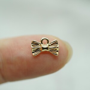 May include: A gold-colored bow tie charm with a loop for attaching to a necklace or bracelet.