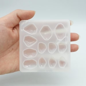 May include: A clear silicone mold with 10 individual cavities shaped like irregular gemstones. The mold is designed for creating resin jewelry or other crafts.