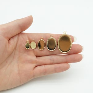 Puede incluir: Una colección de bandejas colgantes ovaladas doradas de varios tamaños. Cada bandeja tiene un lazo en la parte superior para sujetar a una cadena o cordón. Las bandejas están vacías, listas para ser rellenadas con resina, fotos u otros elementos decorativos.