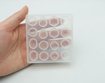 Könnte beinhalten: Eine transparente Silikonform mit 16 einzelnen Vertiefungen, jede in Form einer Blume oder eines kleinen Kreises. Die Form ist zum Erstellen kleiner Kunsthandwerke aus Harz gedacht.