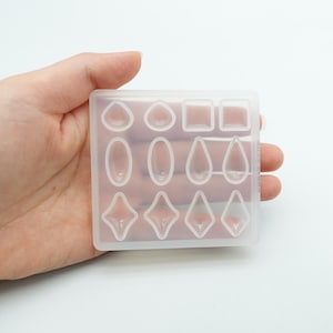 Könnte beinhalten: Transparente Silikonform mit 12 verschiedenen Formen zum Gießen von Harz. Die Formen umfassen Kreise, Ovale, Tropfen und Diamanten.