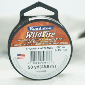 以下が含まれることがあります： フロスト/ブラン/ブランコ色のBeadalon WildFire熱結合ビーズ織り糸のスプール。スプールは黒で、赤とオレンジの炎のデザインが施されています。ラベルには、糸の厚さが0.006インチまたは0.15ミリメートル、長さが50ヤードまたは45.8メートルであることが記載されています。