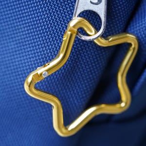 May include: A gold star-shaped zipper pull attached to a blue fabric bag.