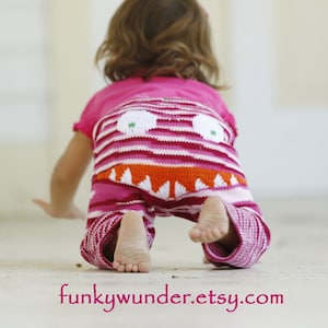 Puede incluir: Un niño o niña lleva pantalones de rayas rosas y blancas con un diseño de cara de monstruo. Los pantalones tienen una boca naranja brillante con dientes blancos y ojos verdes. El niño o niña está gateando en un suelo blanco. El texto "funkywunder.etsy.com" es visible en la parte inferior de la imagen.