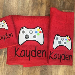 May include: Three red towels with embroidered gray video game controllers and the name "Kayden" in black.