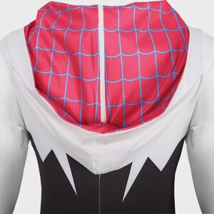 May include: A long-sleeved hooded garment featuring a white upper section and a black lower section with jagged white accents. The hood interior is bright pink with a blue web pattern, and the hood features a central white vertical seam detail.