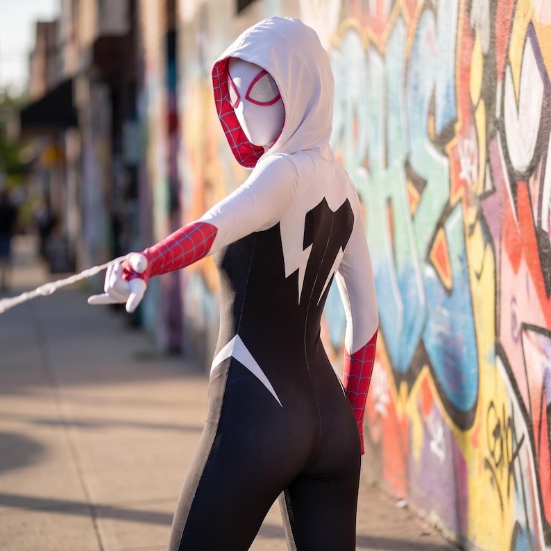 May include: A full-body hooded bodysuit featuring a white hood with a pink web pattern interior, a white torso and arms, and a black lower body. The sleeves have a red and blue web pattern, and the mask is white with pink-rimmed eyes.