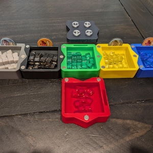 May include: A set of seven colorful trays with magnetic lids. Each tray contains small plastic tiles in different colors. The trays are arranged in a row on a wooden surface.