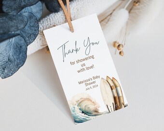 May include: A white thank you tag with blue and brown watercolor illustrations of surfboards and a wave. The text reads "Thank You for showering us with love! Marissa's Baby Shower July 5, 2024".