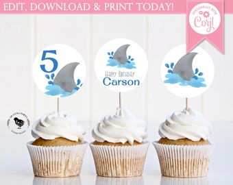 May include: Three cupcakes with blue and gray shark fin cupcake toppers. The toppers have the number "5" and the words "Happy Birthday Carson".
