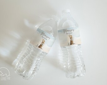 Op de afbeelding: Twee doorzichtige plastic waterflessen met blauwe en witte etiketten waarop "Marissa's Baby Shower" staat. De etiketten tonen een aquarelontwerp van surfplanken.