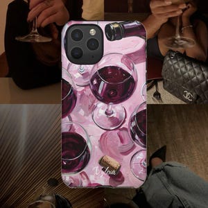 Könnte beinhalten: Eine rechteckige Smartphone-Hülle mit einer gemalten Illustration von mehreren Weingläsern gefüllt mit Rotwein, einem Weinflaschenhals und einem Korken auf rosa Hintergrund. Der Text Vylexa ist unten mittig in weißer Schreibschrift gedruckt.