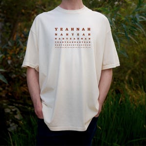 Peut inclure: Un t-shirt crème avec un imprimé graphique brun du texte "YEAHNAH NAHYEAH NAHYEAHNAH YEAHYEAHYEAHNAH NAHYEAHNAHYEAH YEAHYEAHNAHYEAH"