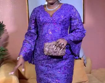 Puede incluir: Una mujer con un vestido de encaje morado, un turbante azul y un pequeño bolso de mano dorado.